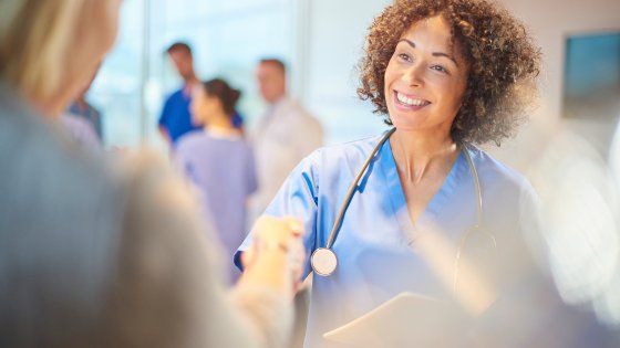 A Nurse wearinga blue Leadcare Recruitment Northern Ireland Uniform, shaking a hand of a male patient.