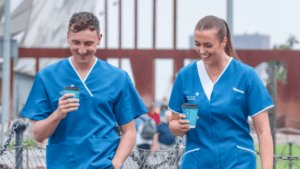A Male and Female Leadcare Nurses wearing their blue uniform, walking in Belfast with a coffee