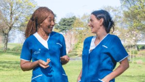 Two female Leadcare Nurses in blue uniform laughing in conversation in Northern Ireland.