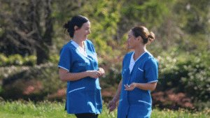 Two female Leadcare Nurses in blue Leadcare scrubs standing together during their lunch break, smiling outside a healthcare facility in Northern Ireland.
