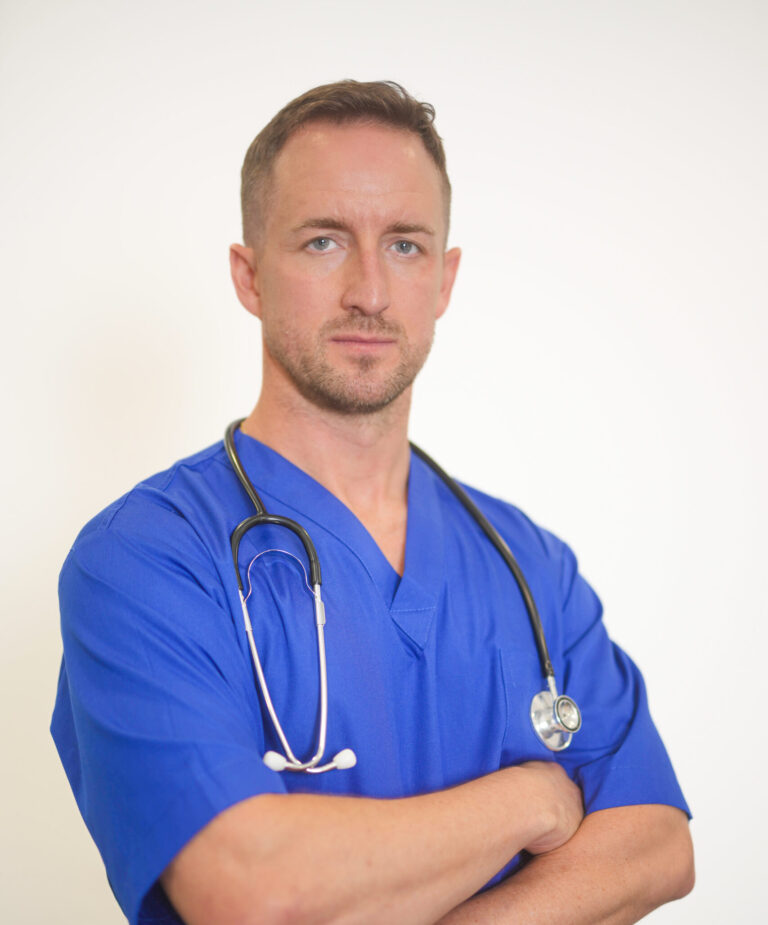 Male nurse in blue scrubs with a stethoscope, arms folded